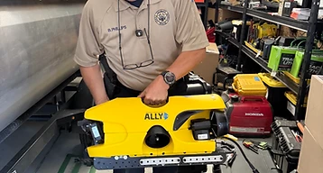Colorado Parks and Wildlife officer holding a yellow underwater remotely operated vehicle (ROV) labeled ALLY.