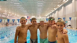 Five young swimmers with arms around each other's shoulders at the pool