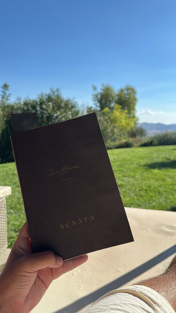 A hand holding a dark hardcover book titled The Book, Susafa, Since 1870