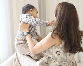 A mother lifting her baby, both dressed in soft neutral pieces
