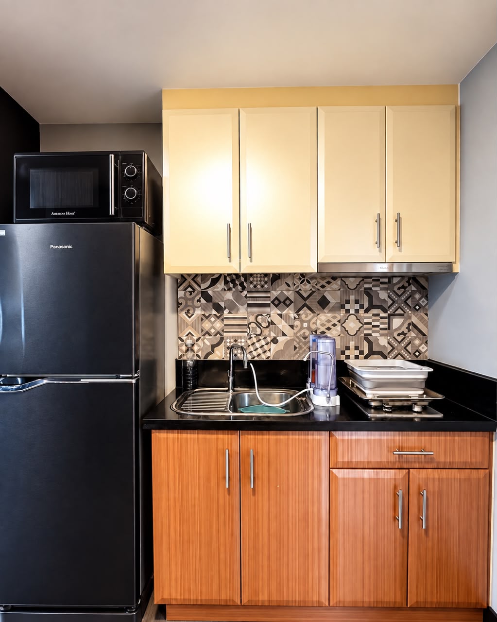 Complete kitchenette with black refrigerator, microwave, range hood, mosaic backsplash, and granite counter