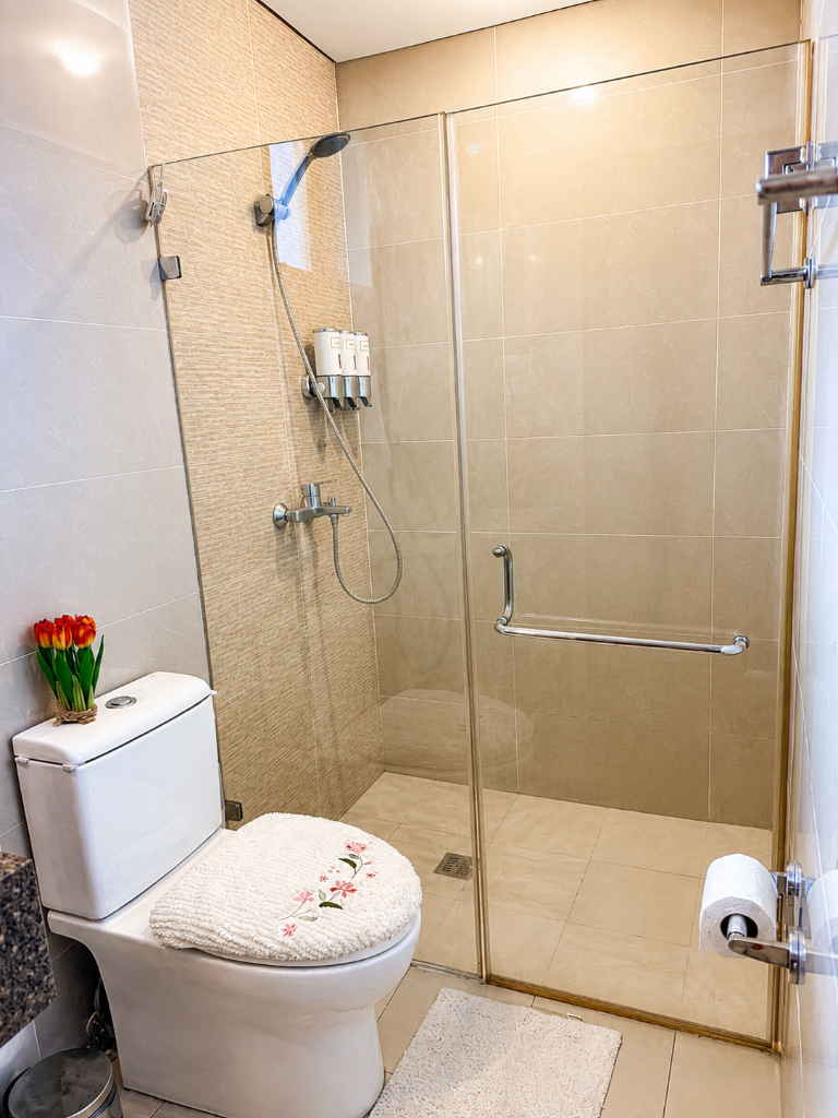 Bathroom with glass shower enclosure, toiletries dispenser, and floral tulip accent