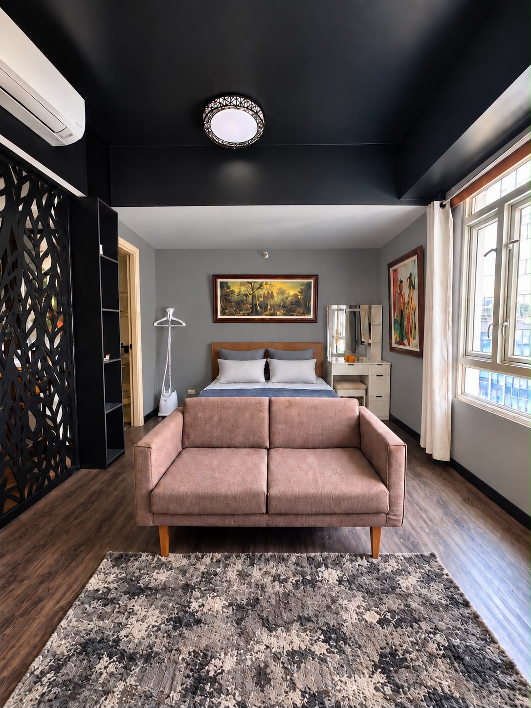 Briana's Haven Three — wide studio view with dusty-rose loveseat, queen bed, vanity, and black laser-cut divider in Newport City