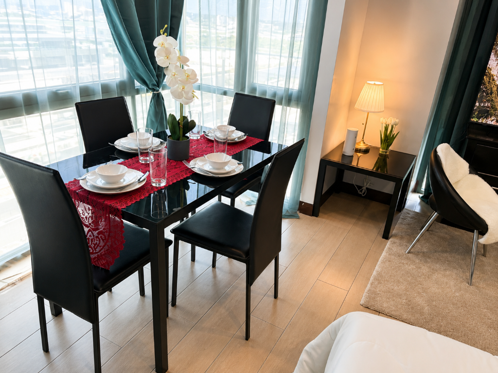Dining area close-up — glass table with four chairs, white orchid centerpiece, and teal drapes