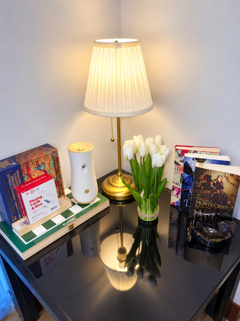 Reading nook with books, board games, white tulips, and warm brass lamp