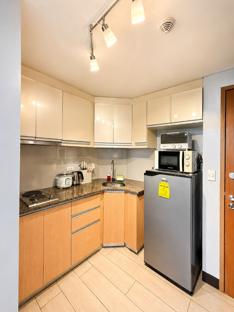 Full kitchen with granite countertops, L-shaped cabinets, refrigerator, microwave, and rice cooker