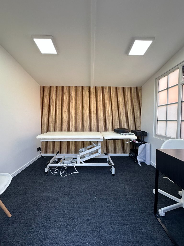 Resolve Movement treatment room with a therapy couch set against a warm wood-slat feature wall and frosted window
