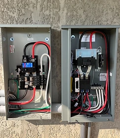 Two open grey electrical enclosures mounted on a stucco wall, showing a panel with Eaton breakers and a transfer switch with standby and normal wiring