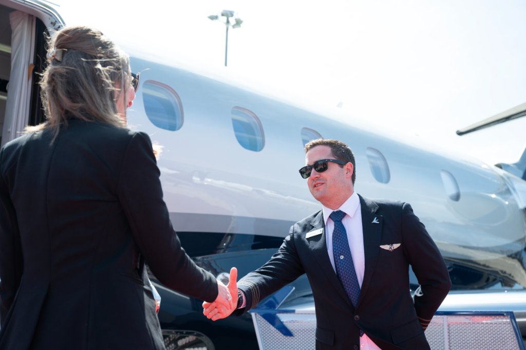 Welcome on board — pilot greeting passenger on the tarmac beside a private jet
