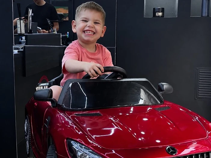 Niño en coche Mercedes-Benz durante su corte de pelo en Why Not Barbershop Barcelona