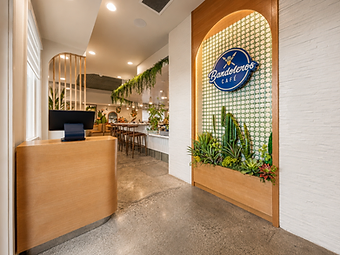 Entrance and reception area of Bandoleros Cafe in Cypress, CA with curved oak host desk, arched niche with backlit Bandoleros logo, geometric green tile, and built-in succulent planter — restaurant interior design by Studio Fridae