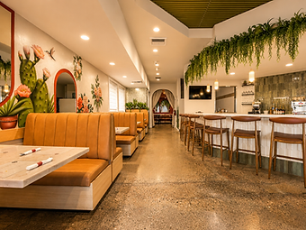 Bandoleros Cafe dining room in Cypress, CA with tan leather booths, marble-topped tables, bar with hanging greenery, and cacti mural — restaurant interior design by Studio Fridae
