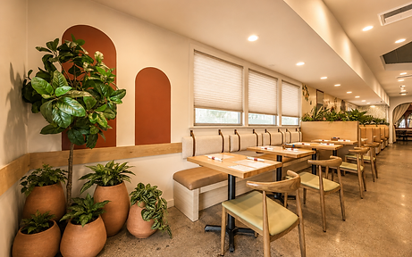 Dining area of Bandoleros Cafe in Cypress, CA with indoor plants, terracotta arch wall accents, light wood wainscot, and tan leather banquette seating — restaurant interior design by Studio Fridae