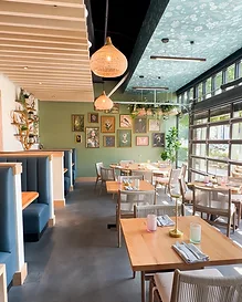 Wide-angle view of Flora dining room with navy booths, gallery wall, and garage-door windows — hospitality interior design in Charlotte, NC by Studio Fridae