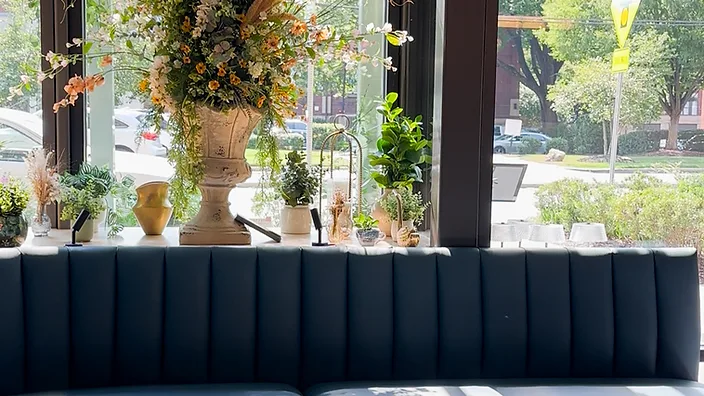 Moody teal booth seating area with floral arrangement and marble bistro tables by window — restaurant interior design in Charlotte, NC by Studio Fridae
