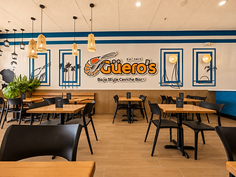 Güero's San Bernardino interior — Baja Style Ceviche Bar restaurant design in San Bernardino, CA with orange Güero's logo wall, blue-framed art, and woven pendant lights by Studio Fridae