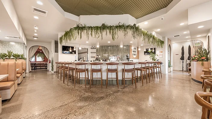 Bandoleros Cafe main dining area in Cypress, CA with hexagonal service bar, hanging greenery installation, and brown leather bar stools — restaurant interior design cost example by STUDIO FRIDAE