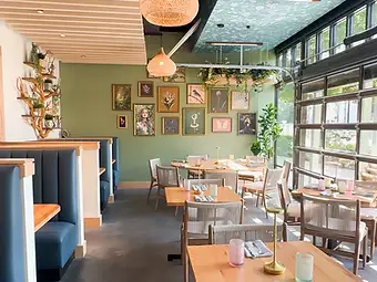 Hospitality interior design by Studio Fridae — Flora dining room in Charlotte, NC with sage-green gallery wall, navy booths, and natural light from garage-door windows