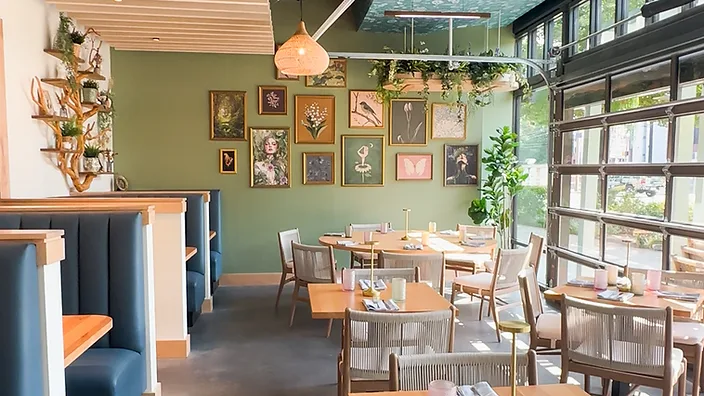 Wide-angle view of Flora dining room with navy booths, gallery wall, and garage-door windows — hospitality interior design in Charlotte, NC by Studio Fridae