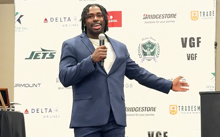 Elijah Green speaking on stage at a corporate summit event in a navy suit