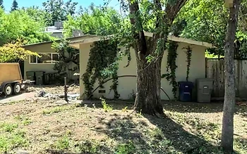 The house as Sean found it: overgrown yard cleared to dirt, ivy climbing the walls, debris and a dumpster trailer in the side yard