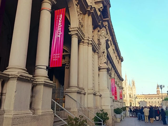 Classical stone colonnade featuring bright pink banners and a distant cathedral view.
