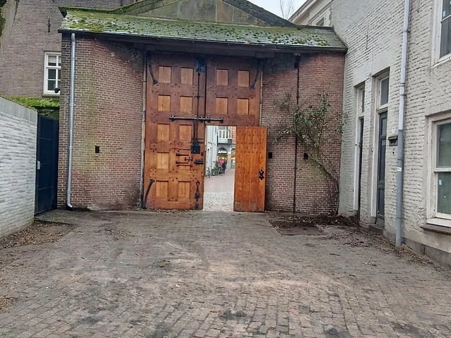 Large wooden gates open from a brick courtyard toward a historic town street view.