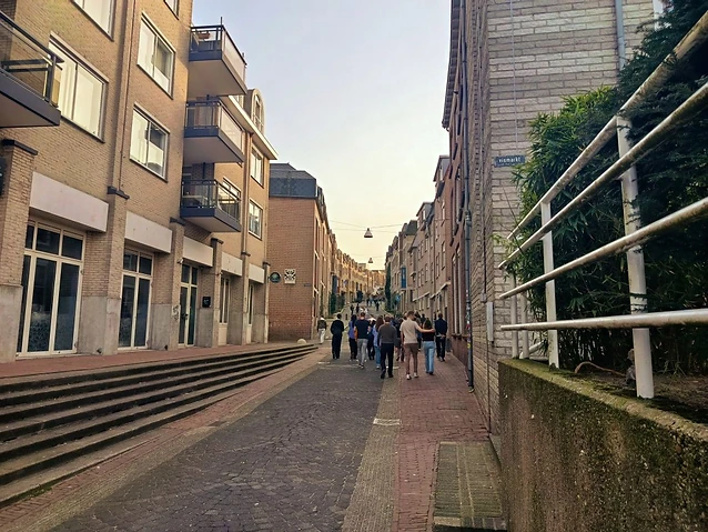 Pedestrians walk up a sloped street flanked by modern apartment buildings.