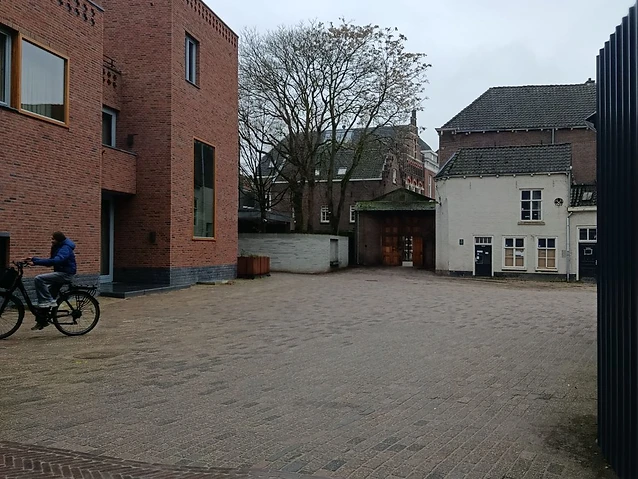 A cyclist rides through a brick courtyard beside a contemporary textured red brick building.