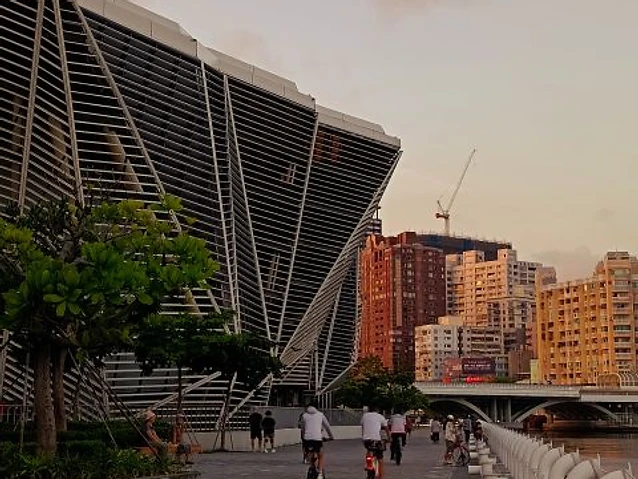 Cyclists and pedestrians move along a paved waterfront path beside the iconic building.