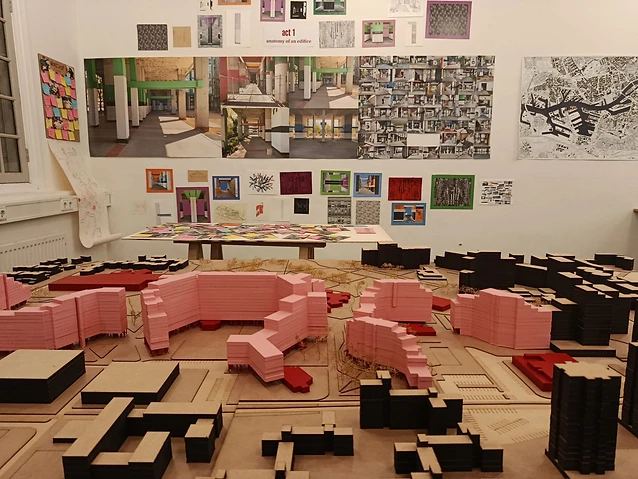 The observer examines an urban model and mounted architectural collage in a gallery.