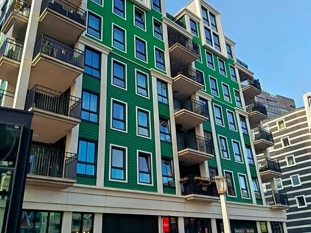 A bright green multi-story residential building with private balconies and ground-floor retail storefronts.