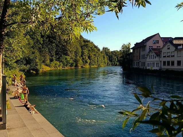 Sunlit concrete steps along a riverbank with people lounging near the water.