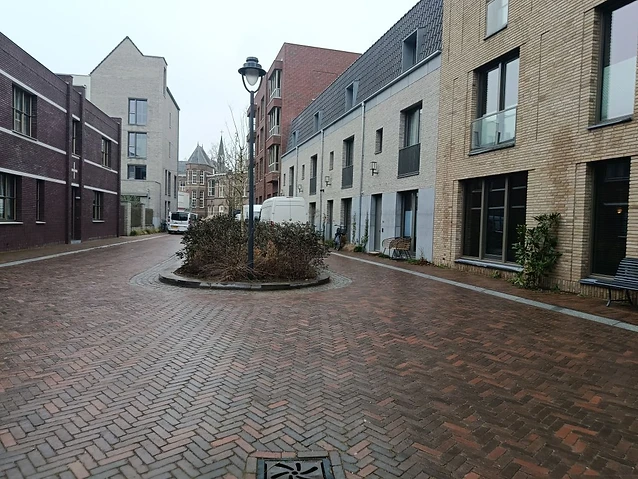 The designer observes brick facades and a small central planting bed in a quiet courtyard.