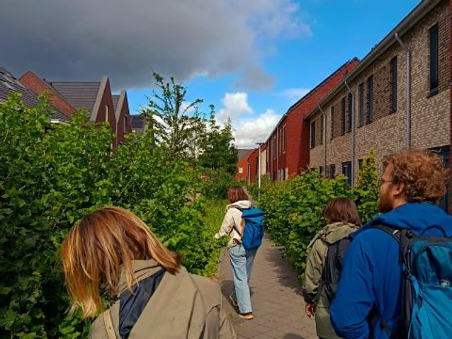 The designer and colleagues walk along a paved path bordered by lush shrubs.