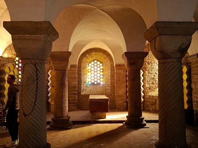 The designer stands inside a dimly lit stone crypt with patterned vaulted ceilings.