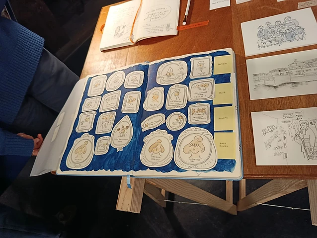 The observer reviews a hand-illustrated sketchbook on a wooden table at the exhibition.