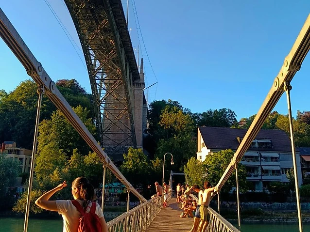The observer on a suspension bridge viewing the river while others lean nearby.