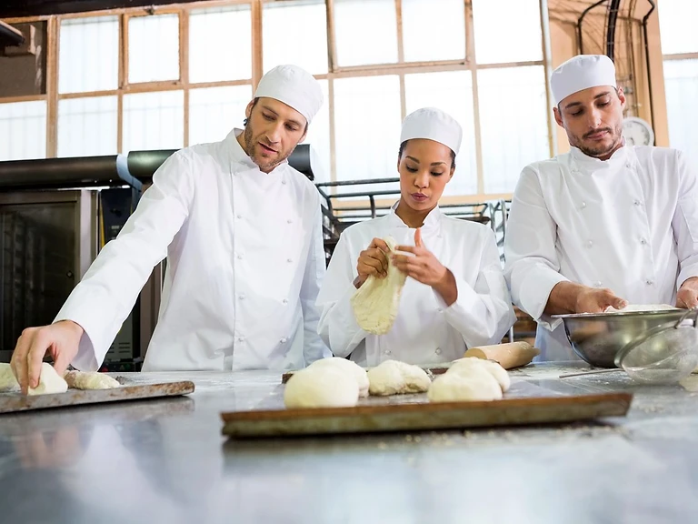 Three bakers working together in a commercial bakery