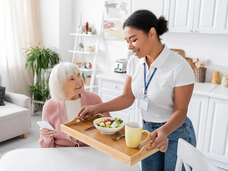 A caregiver serving a meal to an elderly woman in her home