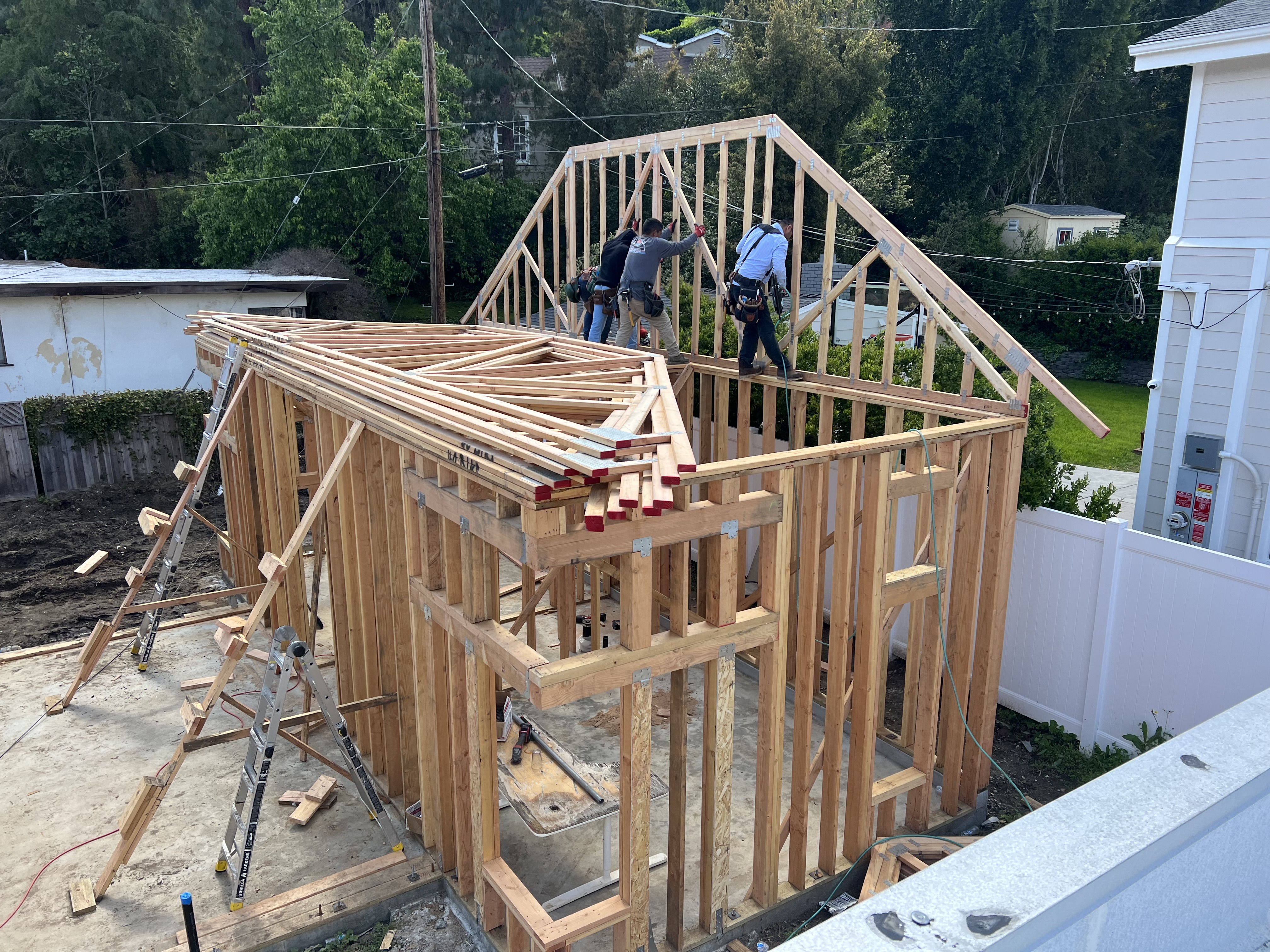 Crew on the roof peak installing rafters with ladders against the frame