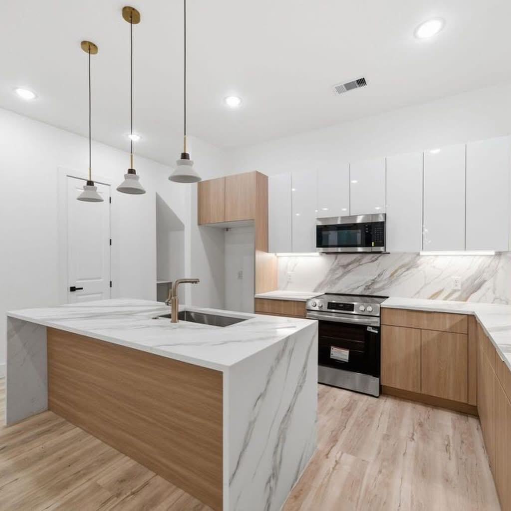 Modern L-shaped kitchen with white upper cabinets, light wood lower cabinets, and gold pendant lights