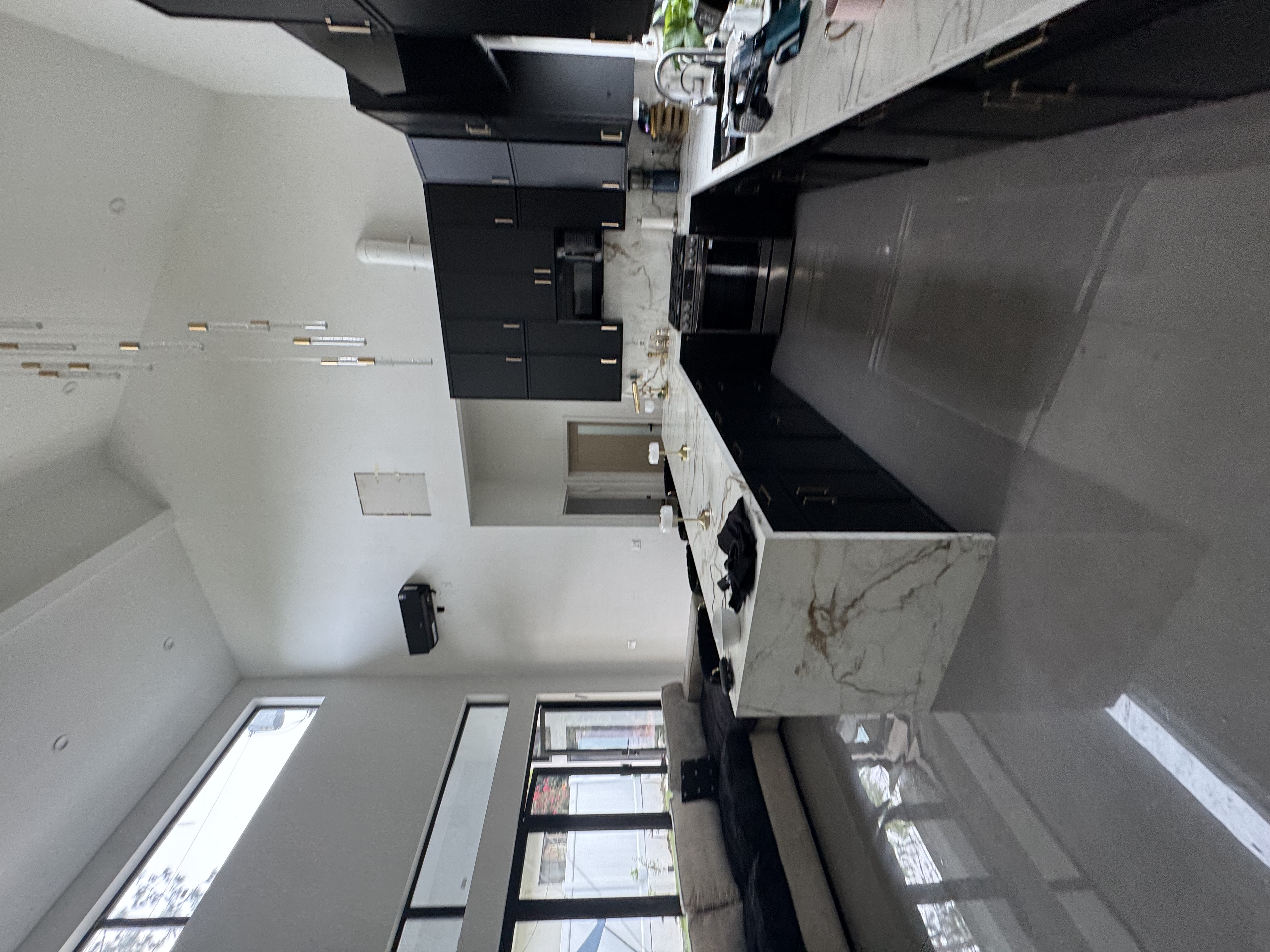 High-end kitchen with matte charcoal cabinetry, linear gold pendant lights, and waterfall island