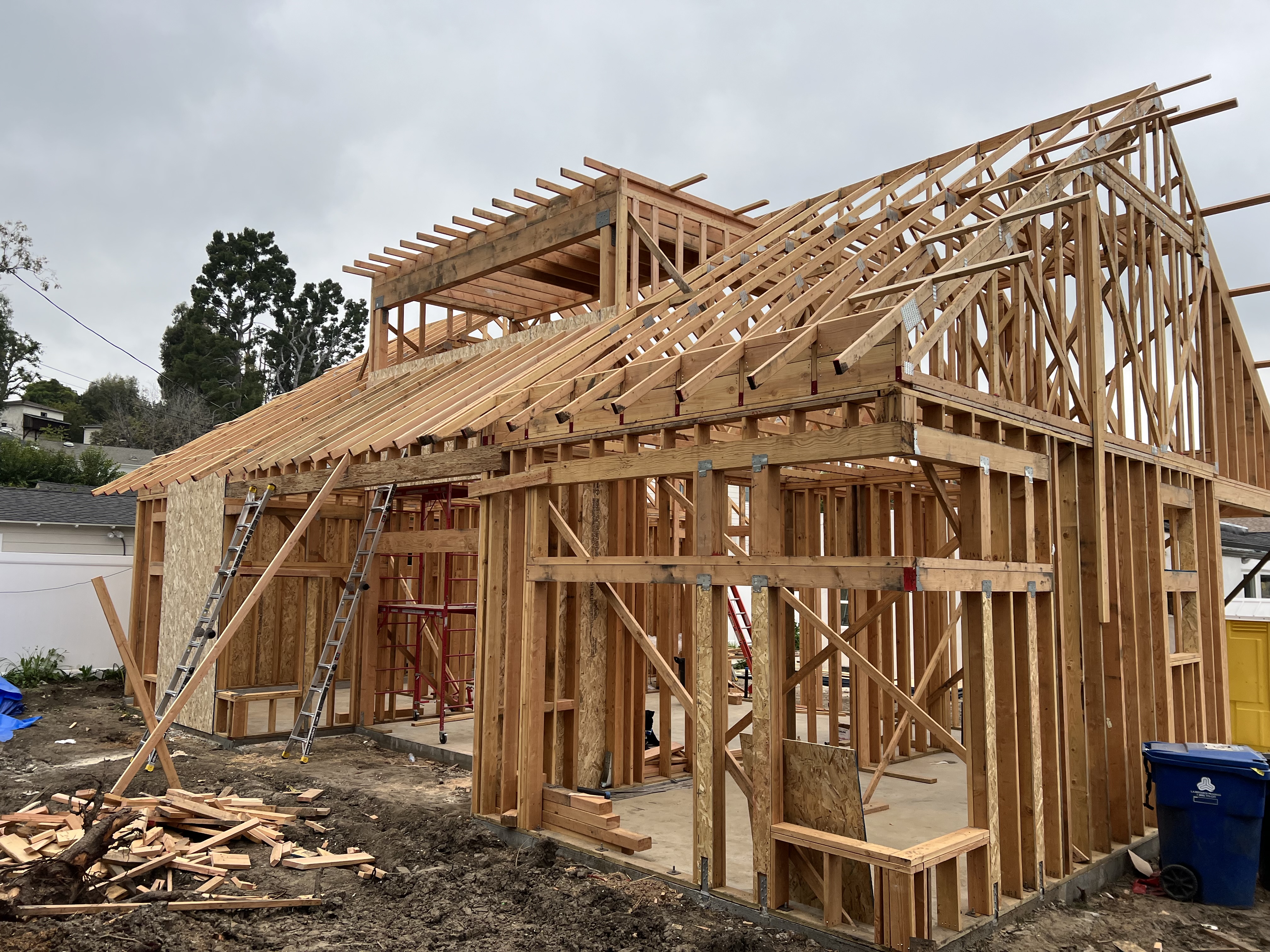 Single-story ADU wood frame in early construction with ladders and waste bin