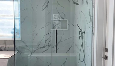 Frameless glass walk-in shower with marble-look tile, rain head, and built-in niche