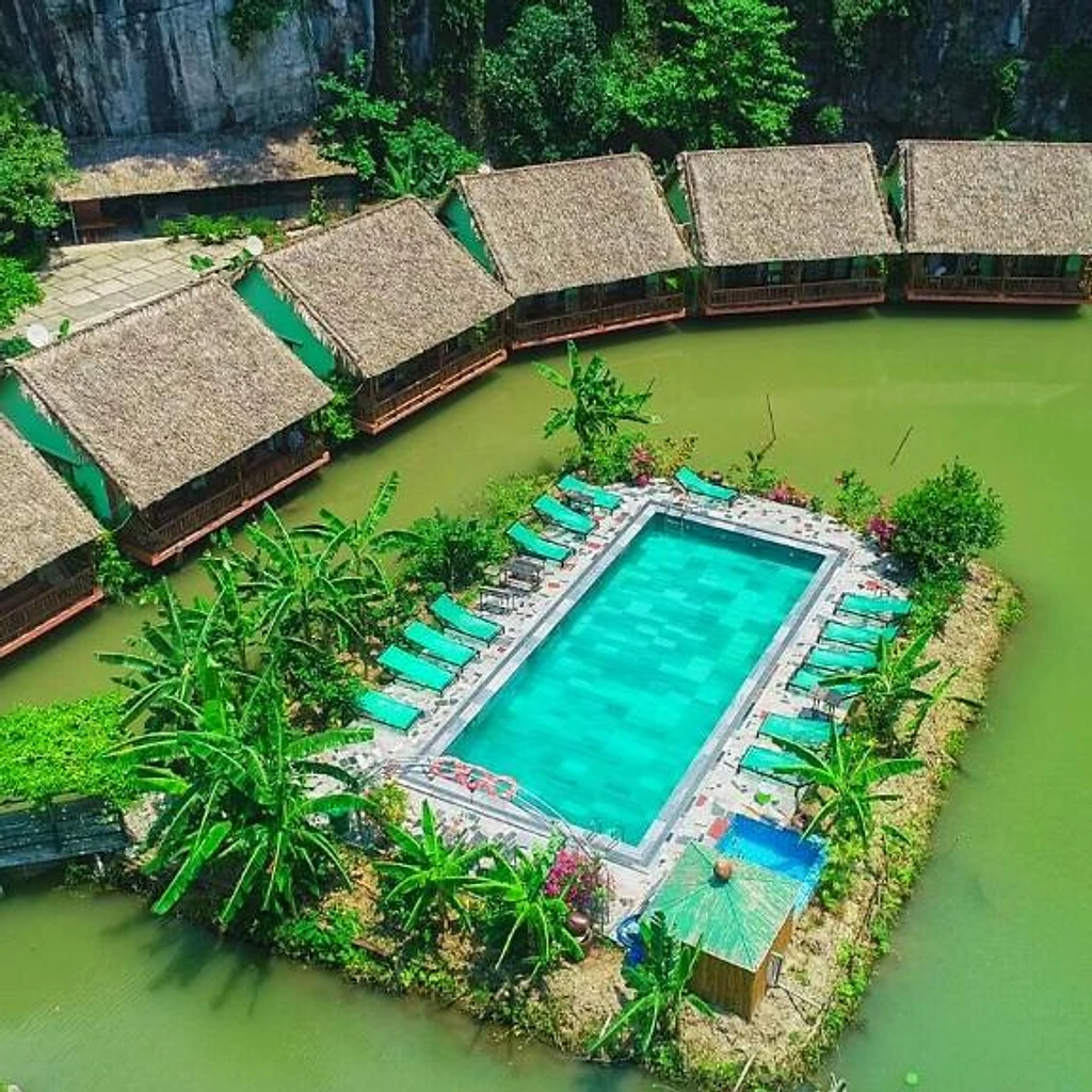 Aerial view of Tam Coc Nature โ pool and thatched bungalows surrounded by water and limestone cliffs