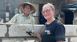 A traveller laying a cinder block alongside a local builder