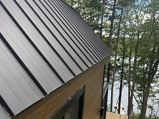 Modern cabin with a standing-seam roof and wooden deck overlooking a lake