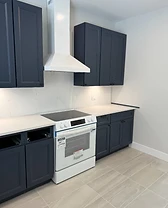 Modern kitchen with navy shaker cabinetry, white range hood, and light stone countertops