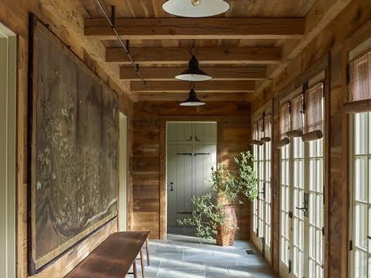 A warm wood-panelled hallway with stone floors and tall windows leading towards distant doors